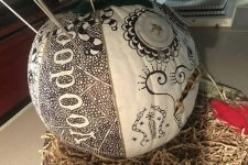 a white pumpkin decorated with a black sharpie with words, patterns and snakes and with some metal sticks is a unique solution