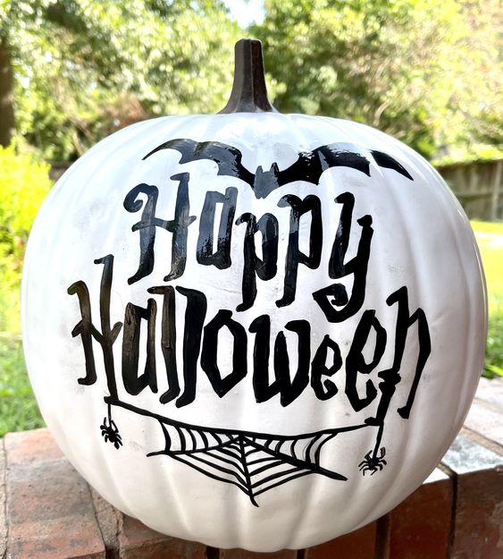 a white pumpkin decorated with black words, bats and spiderwebs is a cool idea for Halloween