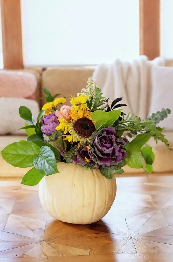 a white pumpkin with foliage, faux yellow and purple blooms and some dried touches is a chic fall centerpiece