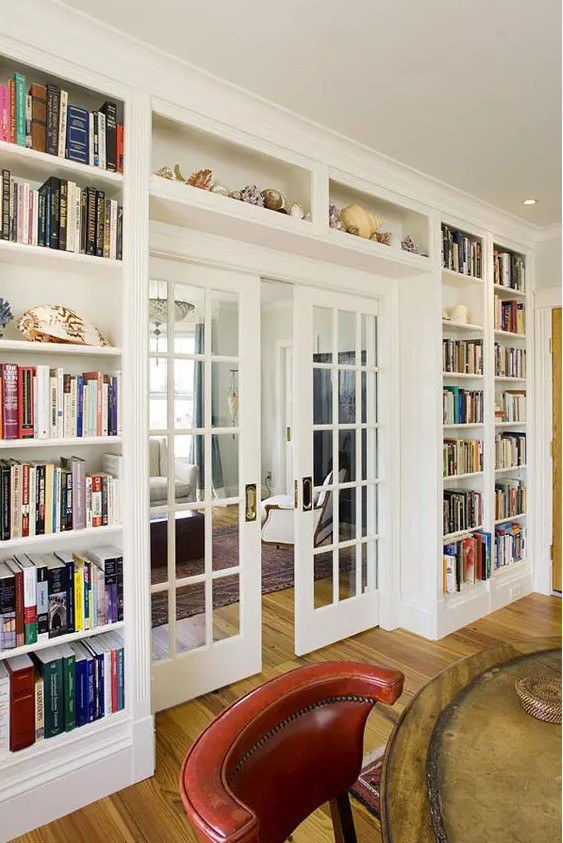 a whole wall taken by lots of open bookshelves on the sides and over the door, with a glass French door is a cool idea to store books and do that with style