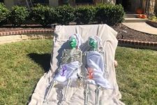 a yard skeleton scene with two skeletons relaxing with masks on their faces is a cool idea for Halloween