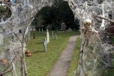 a yard turned into a graveyard, with a branch and spiderweb arch plus some skeletons for yard decor