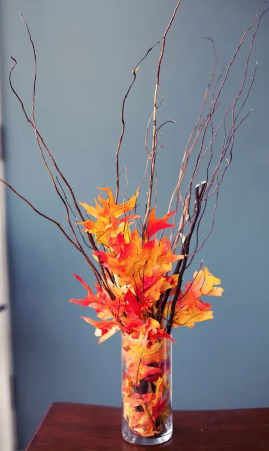 an easy and budget-friendly fall centerpiece of twigs and bright faux leaves in a vase to make last minute