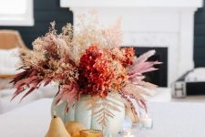 an eye-catching fall flower arrangement with both dried and fresh blooms, with bright spray painted leaves and fruit