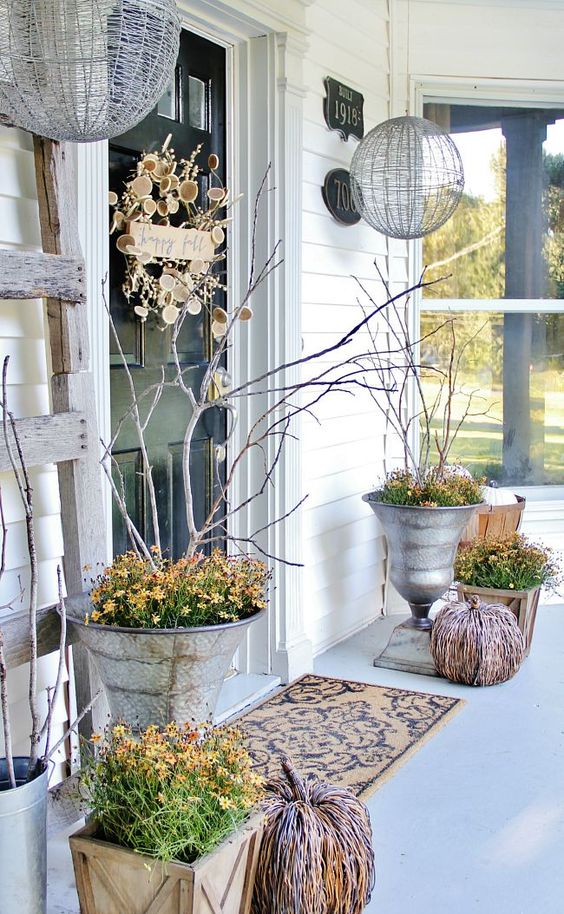 lovely rustic fall decor for the porch, with vine pumpkins, bold blooms, branches and twigs an a creative wreath on the door