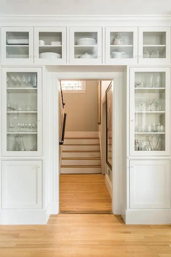 Off white storage units surrounding the doorway completely to provide space for glassware and porcelain is amazing