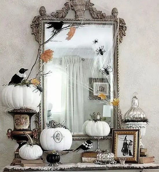 vintage Halloween decor with a large mirror in an ornated frame, white pumpkins with patterns and blackbirds plus spiders and fall leaves