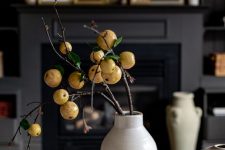Scandinavian fall decor with a color block vase and branches with fruit, wooden chain and some bowls