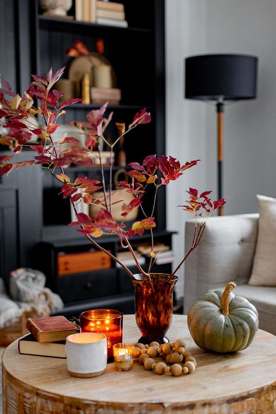 Scandinavian fall decor with an amber vase and bold leaves, a pumpkin, beads, books and candles