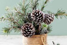 a Christmas centerpiece of a can wrapped with burlap, snowy pinecones, evergreens is a cool idea for a rustic space