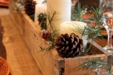a Christmas centerpiece of a wooden box, evergreens, pinecones and pillar candles is very cozy