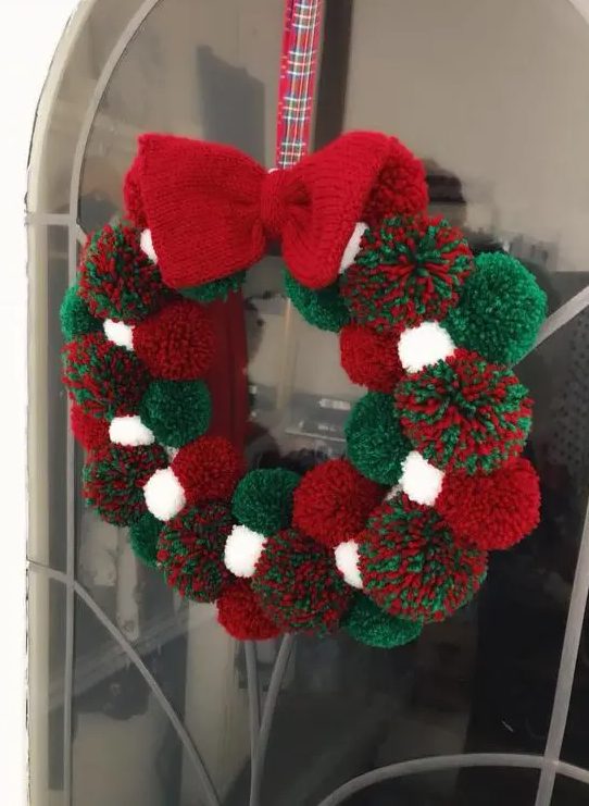a Christmas pompom wreath of white, green and red pompoms and a knit bow