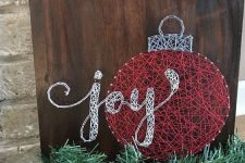 a Christmas string art piece showing an ornament and claligraphy, done with red and white yarn