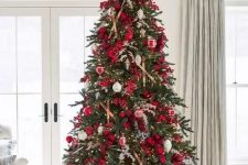 a Christmas tree decorated with lights, red berries, branches, plaid ribbons, red and white ornaments is amazing