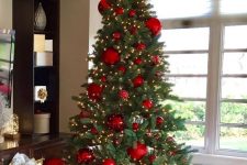 a Christmas tree with oversized red ornaments, berries on top and lights is a bold and catchy solution