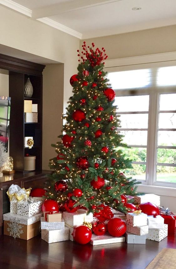 a Christmas tree with oversized red ornaments, berries on top and lights is a bold and catchy solution