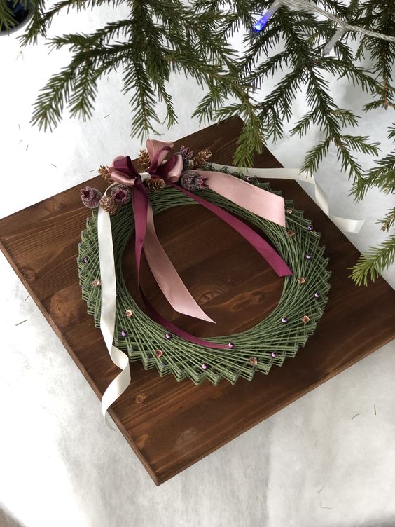 a Christmassy string art showing off a wreath, decorated with pinecones and ribbons, is a cool and catchy idea