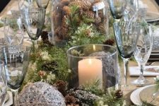 a beautiful Christmas tablescape with pinecones, evergreens, yarn balls, pillar candles, grey and white plates and grey glasses