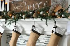 a beautiful rustic Christmas mantel styled with tine balls, silver ornaments, pinecones, evergreens, burlap stockings and wooden plaque Christmas sign
