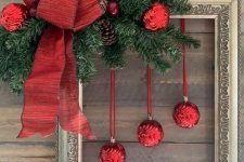 a bold Christmas decoration of a vintage frame, evergreens, red ornaments, pinecones and a large red bow is amazing