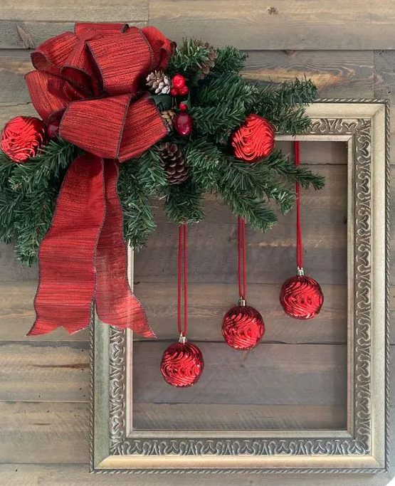 a bold Christmas decoration of a vintage frame, evergreens, red ornaments, pinecones and a large red bow is amazing