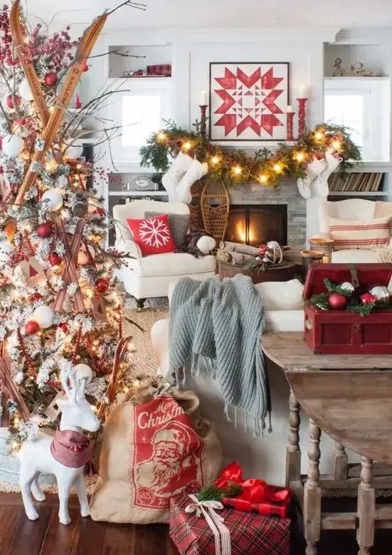 a bold and creative Christmas living room with a white tree with red and white ornaments and skis, a fir garland with lights, red candleholders and a red box with ornaments