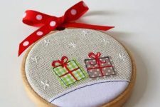 a bright Christmas ornament of an embroidery hoop and some gift applique, with a red bow on top is a cool decoration to DIY