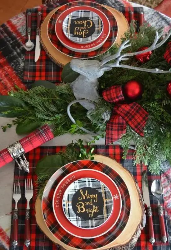 a bright Christmas tablescape with red plaid linens, chargers, ribbon, evergreens and red Christmas ornaments is cheerful