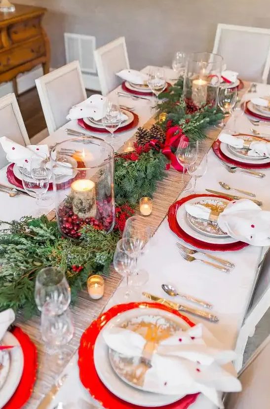 a bright and chic Christmas table setting with evergreens, red berries, candles wrapped with bark, red chargers and polka dot napkins