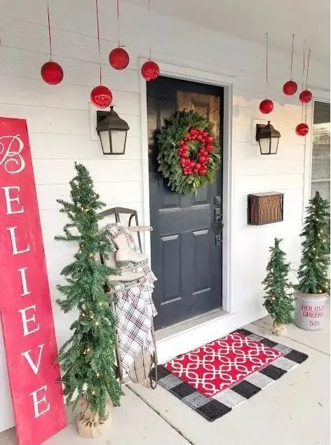a bright and fun Christmas porch with red ornaments, mini lit up Christmas trees, a red sign and layered mats