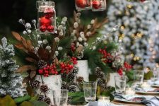 a bright outdoor Christmas tablescape with a paper runner and placemats, buffalo check napkins, bold evergreens, snowy pinecones and berries, red ornaments over the table