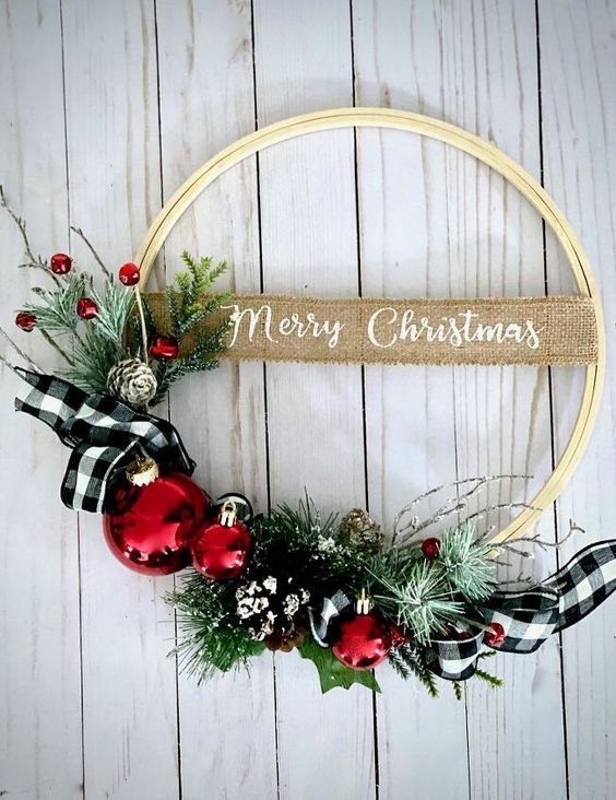 a classy holiday wreath of an embroidery hoop, greenery, berries, red ornaments, evergreens and plaid ribbon