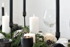 a contrasting Christmas table with an evergreen runner with snowy pinecones, black and white faceted ornaments, black and white candles and white plates plus black napkins