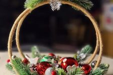 a cool Christmas decoration of two embroidery hoops, evergreens, red and silver ornaments and a bird on top is a lovely idea