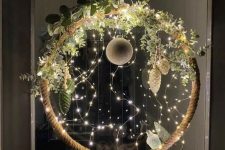 a cool Christmas wreath of an embroidery hoop wrapped with rope, with lights, greenery, pinecone and bauble ornaments