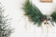 a cool embroidery hoop wreath with greenery, snowy pinecones, a little sign is a cool natural decor idea