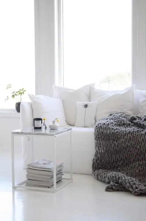 a cozy white nook spruced up with a heavy knit blanket for the fall is a great Nordic inspired idea