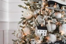 a flocked farmhouse Christmas tree with white ornaments, pinecones, skates, a sign and a house is a lovely idea