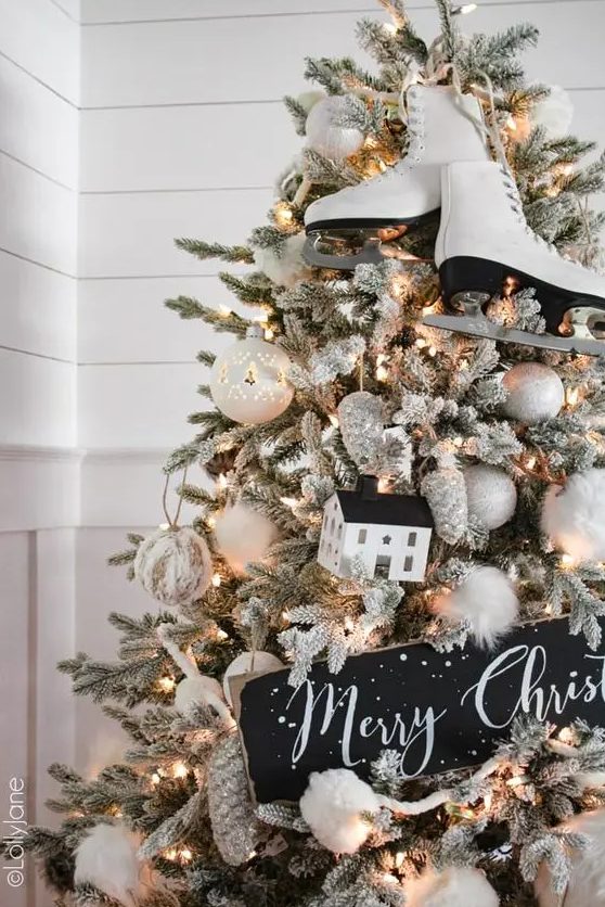 a flocked farmhouse Christmas tree with white ornaments, pinecones, skates, a sign and a house is a lovely idea