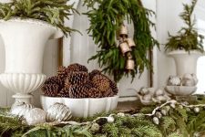 a gorgeous woodland Christmas mantel with evergreens, pinecones, lights, ornaments and bells is awesome