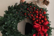 a jaw-dropping Christmas wreath of evergreens, red ornaments from small to large ones and a large red bow