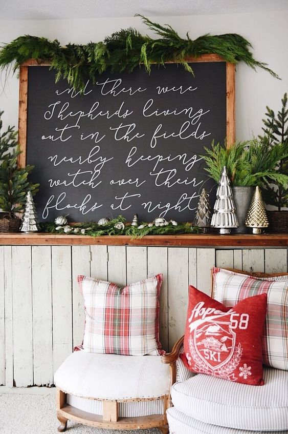 a large hand painted Christmas sign that imitates a chalkboard in a frame, topped with greenery, for a rustic space