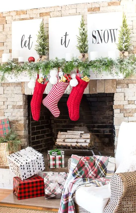 a lovely Christmas mantel with a snowy evergreen garland, red sotckings, ornaments, candles, tree and signs is a very bold and cool idea