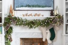 a lovely Christmas mantel with an evergreen and pinecone garland with stars, stockings, mini trees and lots of deer figurines