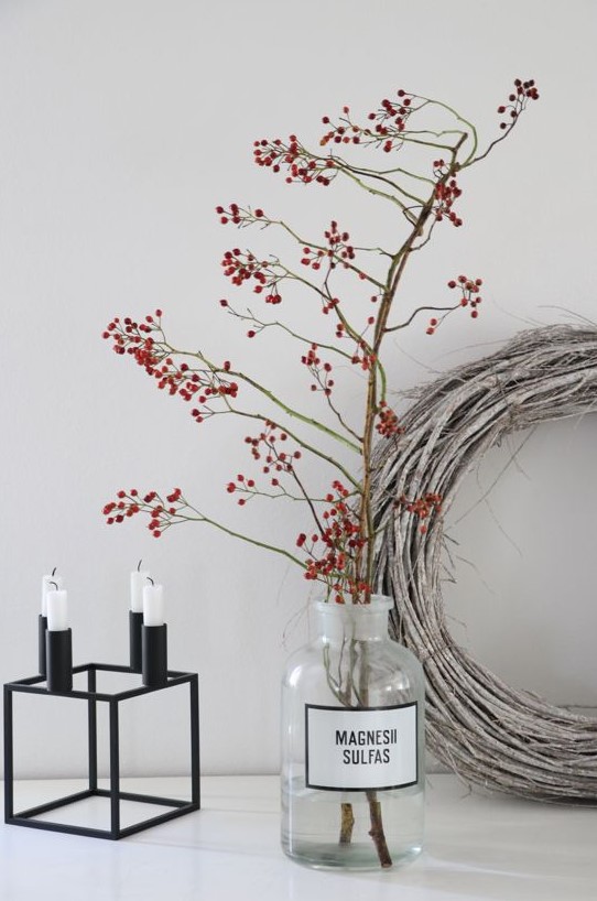 a matte black candelabra with candles, branches with berries in a glass bottle and a whitewashed vine wreath