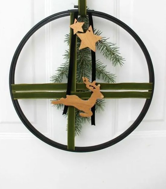 a modern Christmas wreath of an embroidery hoop, green and black velvet ribbons, evergreens, wooden stars and a deer