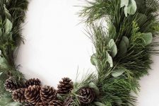 a modern Christmas wreath with evergreens and greenery and pinecones is a cool decoration to rock