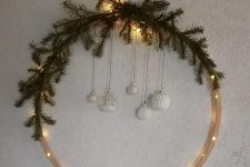 a modern Christmas wreath with lights, evergreens, white ornaments hanging down is a lovely idea for winter decor
