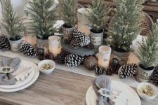 a modern rustic Christmas table with bells, pinecones, potted Christmas trees and wooden tree ornaments plus grey napkins