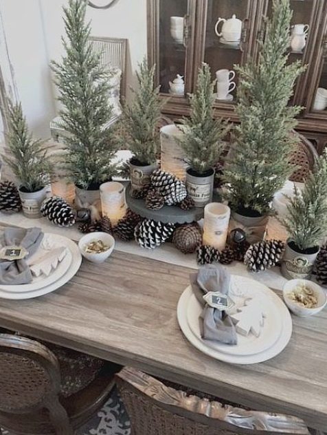 a modern rustic Christmas table with bells, pinecones, potted Christmas trees and wooden tree ornaments plus grey napkins